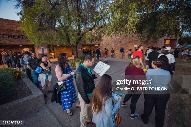 Voters lining up to cast their ballots in person read voting guides handed out by volunteers at the Fowler School polling station in Tempe, Arizona,...