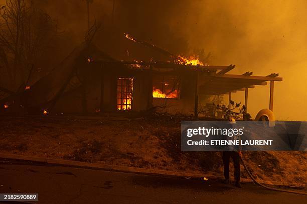 Firefighter pulls a hose in front of a burnt house as the Mountain Fire scorches acres in Camarillo Heights, Camarillo, California, on November 6,...
