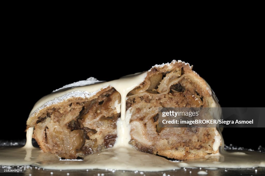 Apple strudel with sultanas, vanilla sauce and icing sugar, studio photography with black background