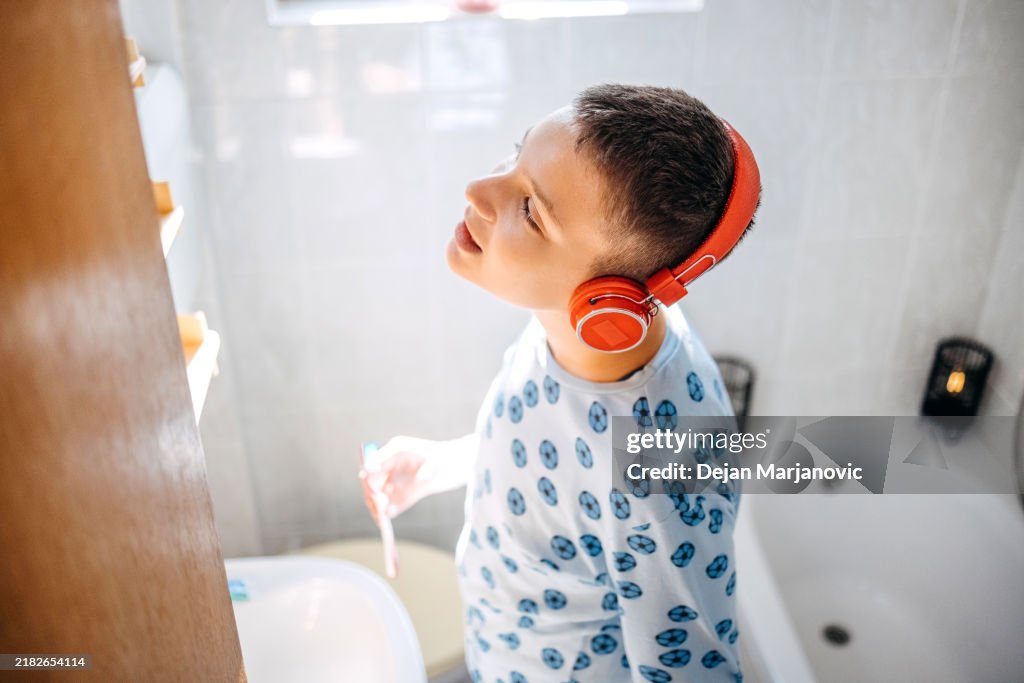 Teenager boy standing in front of mirror in bathroom in morning hours looking at teeth