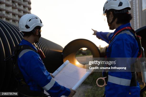 male engineers specializing in pre-construction, along with technicians using safety harnesses, and clear screens are discussing plans to inspect the large drainage pipe work site. - osha hazard communication pictogram stock pictures, royalty-free photos & images
