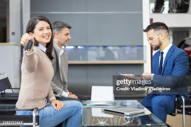 woman sitting with a car salesman at dealership holding car keys with a smile - retail lease sign stock pictures, royalty-free photos & images
