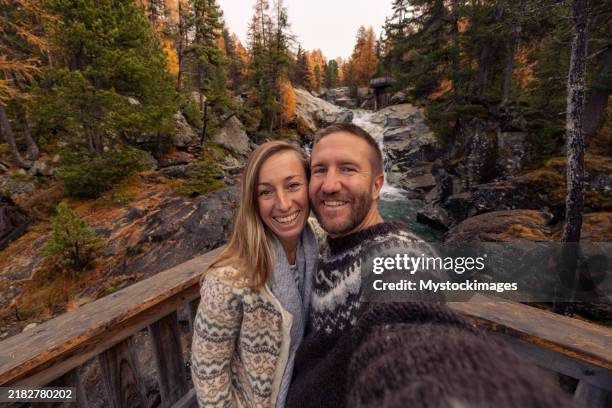 smiling couple taking selfie by autumn waterfall - cardigan sweater stock pictures, royalty-free photos & images