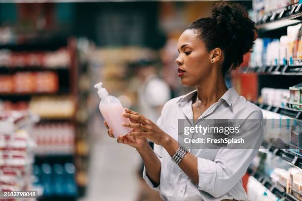 mujer joven que compra productos de belleza en un pasillo de supermercado - artículos de aseo fotografías e imágenes de stock