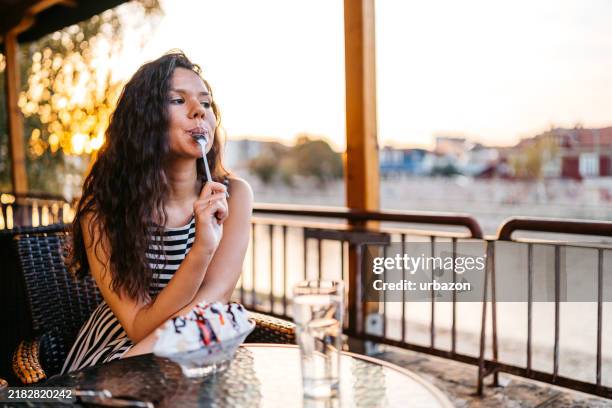 young woman eating banana split by the riverside café - riverbank stock pictures, royalty-free photos & images