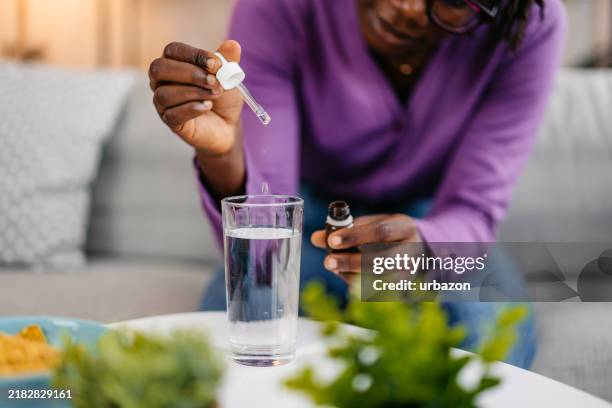 young woman putting medicine drops in a glass of water - black oil in water stock pictures, royalty-free photos & images