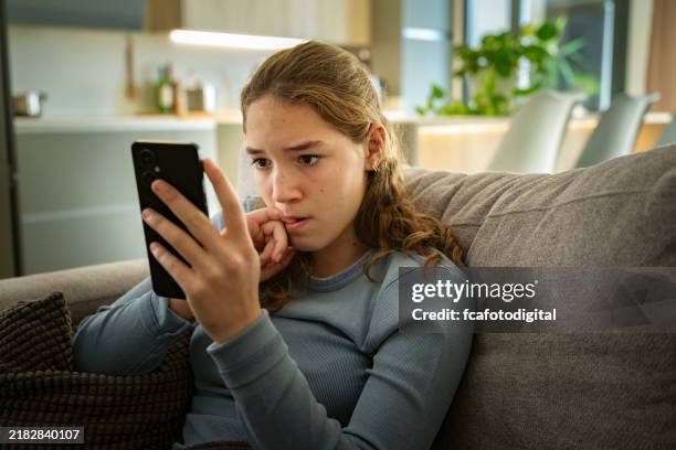 retrato de una adolescente nerviosa que mira su teléfono inteligente mordiéndose las uñas preocupada por las malas noticias - sólo-grupo-de-adolescentes fotografías e imágenes de stock