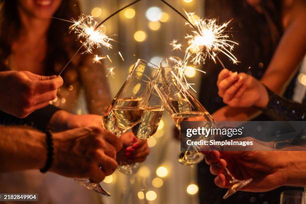 young friends clinking glasses of champagne in a nightclub. group of happy people holding sparklers at the party. celebration, people and holidays concept. - nieuwjaar stockfoto's en -beelden