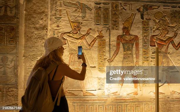 mujer usando un teléfono inteligente y tomando una foto mientras visita las habitaciones interiores dentro del templo de abu simbel, en el sur de egipto en nubia junto al lago nasser. templo del faraón ramsés ii - cultura egipcia fotografías e imágenes de stock