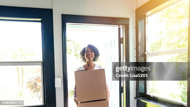 african american woman in her 50’s carrying moving boxes into an empty house after becoming a homeowner - proprietario di casa foto e immagini stock