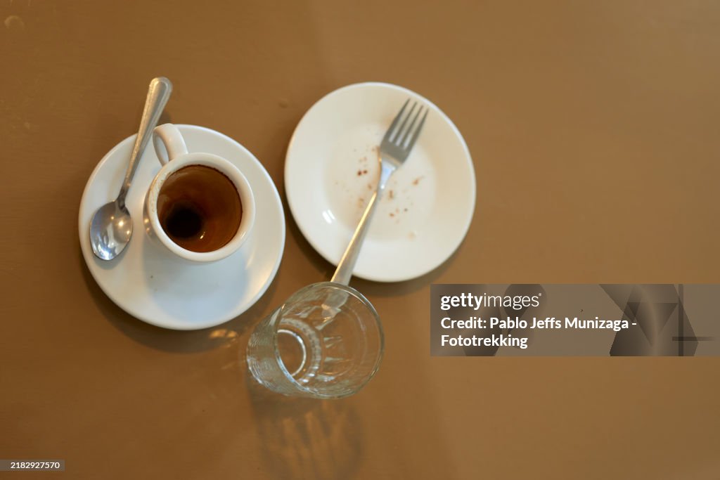 Empty coffee cup, glass, and plate with crumbs on cafe table