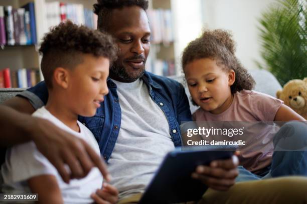 father and his kids using digital tablet in the living room at home - family television stock pictures, royalty-free photos & images