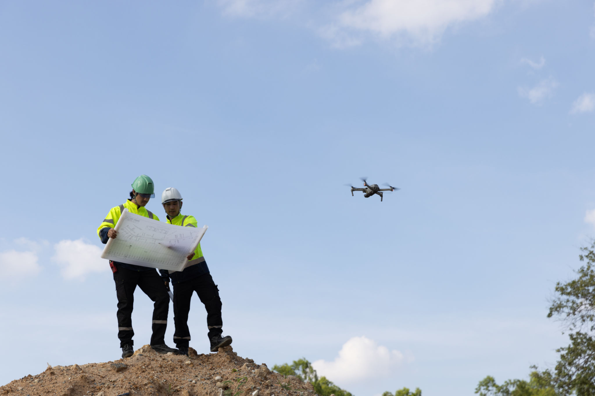 Two male civil engineers stand on a high pile of dirt to survey the area, laying the drainage system with aerial photography equipment as an aid in surveying. Two male civil engineers stand on a high pile of dirt to survey the area, laying the drainage system with aerial photography equipment as an aid in surveying.
