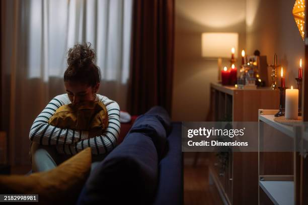 sad young woman hugging pillow on sofa during christmas time - blues stockfoto's en -beelden