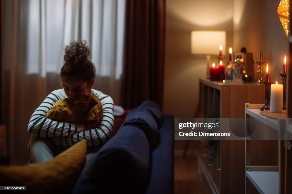 Sad young woman hugging pillow on sofa during christmas time