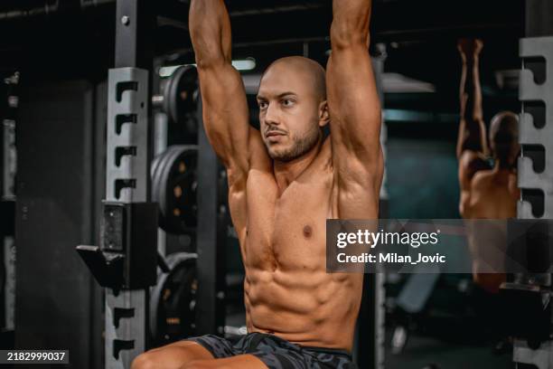muscular build athlete doing abs in a gym. hanging leg raise - beautiful bodybuilders stock pictures, royalty-free photos & images