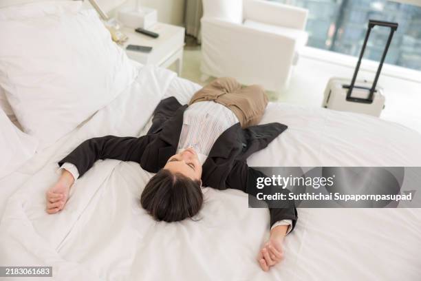 exhausted businesswoman in a hotel room: overworked corporate traveler finds solitude and comfort, lying on a bed to recover after a demanding business trip in a quiet, private space - locket photos stock pictures, royalty-free photos & images