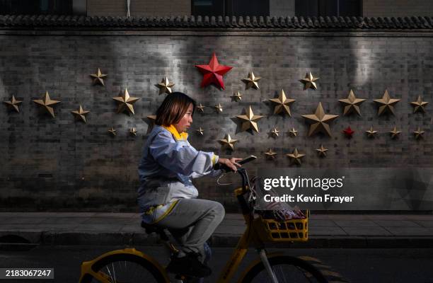 Woman rides a shared bike by a wall of a historic building adorned with a red star in an upscale commercial area on November 5, 2024 in Beijing,...