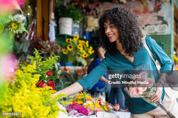 joven viajera examinando los productos expuestos en el mercado de flores de medellín, colombia. - mercado de flores fotografías e imágenes de stock