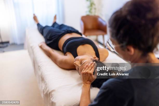 therapist performing face and head massage on patient - chiropractor stockfoto's en -beelden