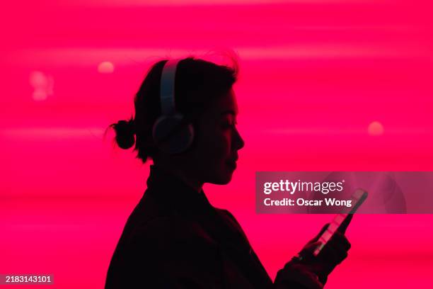 side view of young asian woman in silhouette using smartphone against illuminated red screen - musik bildbanksfoton och bilder