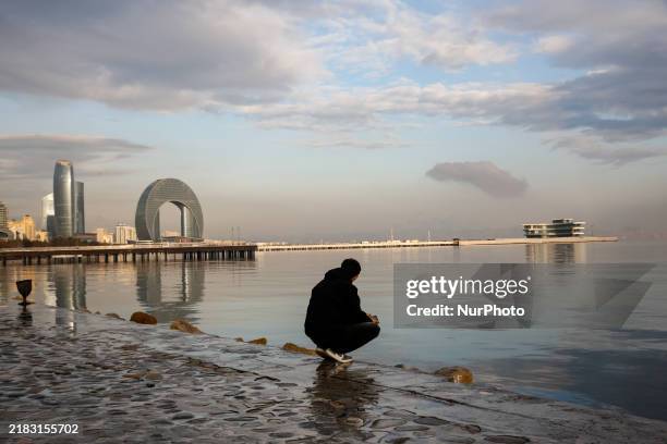 Man sits on Caspian Sea Boulevard in Baku in front of landmark architecture, Azerbaijan on November 9, 2024.