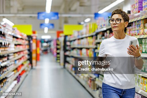 Beautiful lady searching grocery in supermarket following shopping list on smartphone Beautiful lady searching grocery in supermarket following shopping list on smartphone