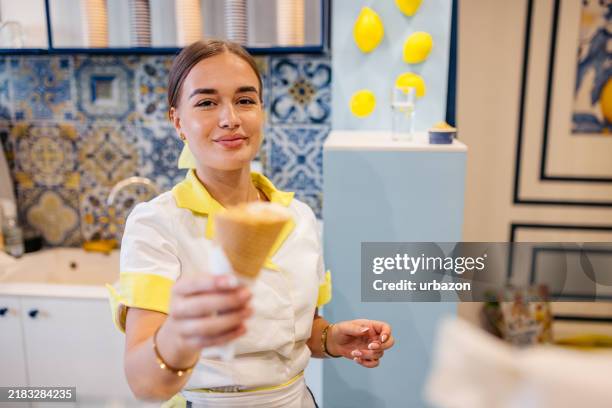 young woman serving a scoop of ice cream in a cone in an ice cream shop - gefrorener joghurt stock-fotos und bilder