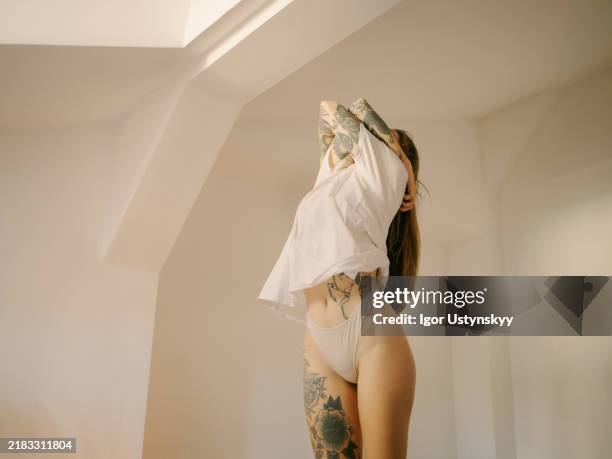 young tattooed woman taking off t-shirt - spogliarsi foto e immagini stock