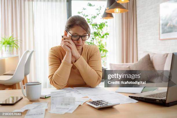 mature woman contempling bills and tax papers at home - debt stock pictures, royalty-free photos & images