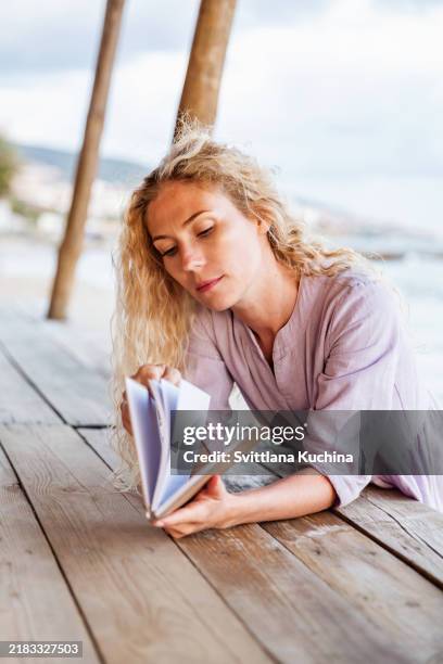 capturing thoughts by the water: woman with notebook at beach - woman reading script stock pictures, royalty-free photos & images