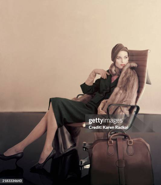 Model seated in an Eames aluminum high backed office chair in front of a tan studio backdrop. She is wearing a mink coat of "Autumn Haze" Emba...