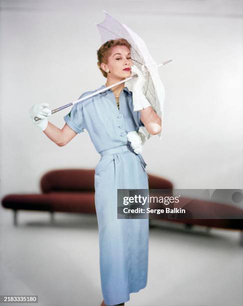 Model Lisa Fonssagrives in a studio near a bulbous, round-edged sofa designed by Isamu Noguchi for Herman Miller, wearing a pale blue silk shantung...