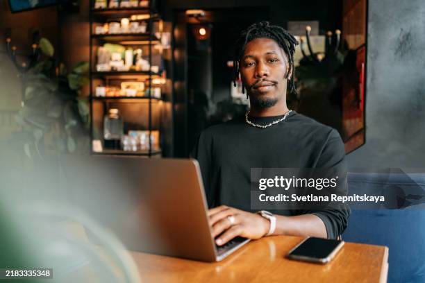 black man with laptop using artificial intelligence while sitting at a table in a cafe while traveling - surfer sur le net photos et images de collection