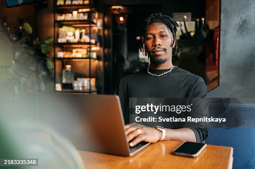Black man with laptop using artificial intelligence while sitting at a table in a cafe while traveling Black man with laptop using artificial intelligence while sitting at a table in a cafe while traveling