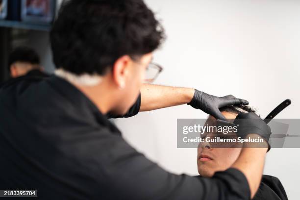 barber shaving eyebrows with a razor - barbier stockfoto's en -beelden