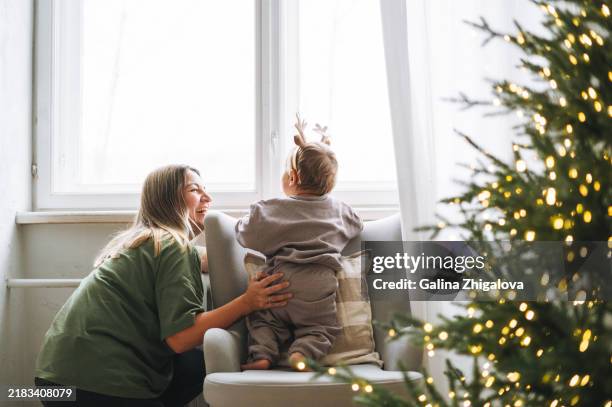 happy woman young mother with cute baby boy on hands near the christmas tree at home - december stockfoto's en -beelden