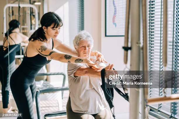 female pilates instructor helping mature woman do exercises on reformer during pilates class. - rehabilitation center stock pictures, royalty-free photos & images