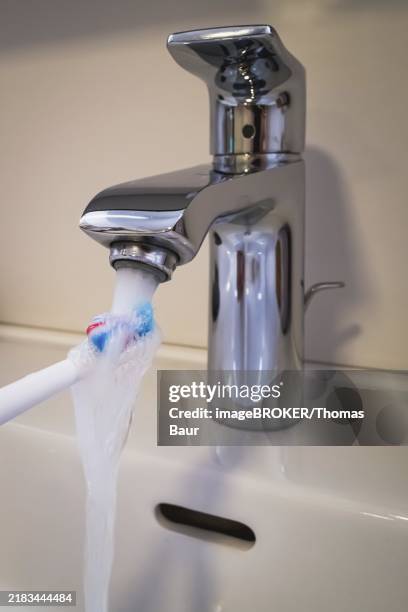 a bathroom tap is running while a toothbrush is held under the running water, symbolic image of water consumption - reflex hammer stock illustrations