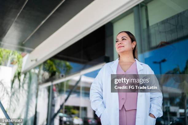 mujer doctora madura contemplando al aire libre - bata de laboratorio fotografías e imágenes de stock