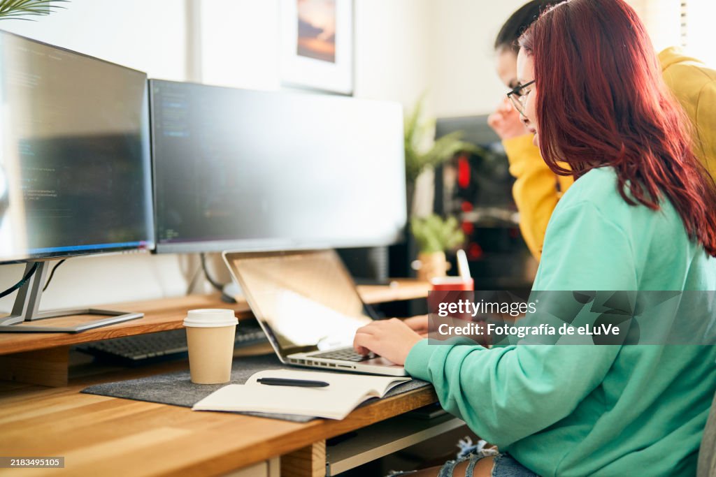 Programmers working together on code using laptop and multiple screens