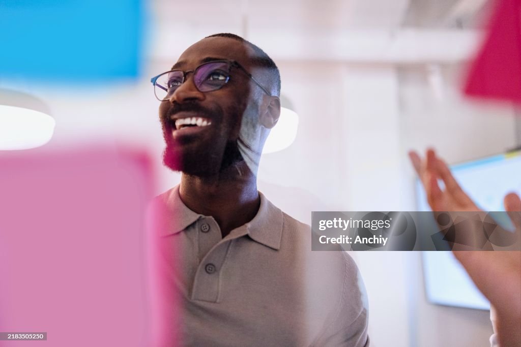 Portrait of a black man presenting his ideas on a glass wall during a business meeting