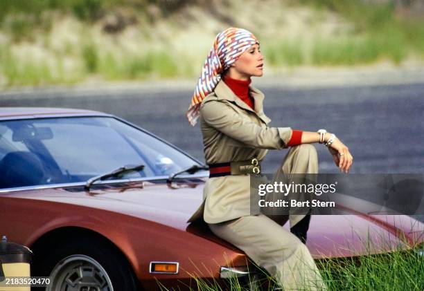 Architect/Model Mazie Cox resting on the hood of a Tomaso Pantera car, wearing a dacron and cotton khaki safari-shirtdress with matching pants and a...