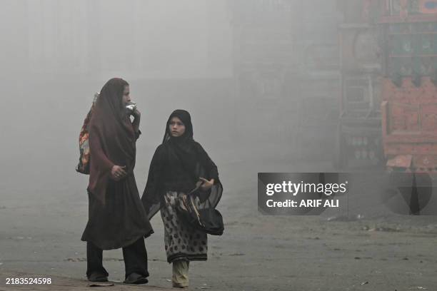 Pedestrians walk along a road engulfed in thick smog in Lahore on November 11, 2024. Lahore, a city of 14 million people stuffed with factories on...