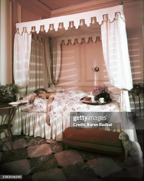 Model sleeping in a circa 1820 French brass four poster canopy bed with handmade French linen sheets by Baccarat and Porthault. She is in a pink room...