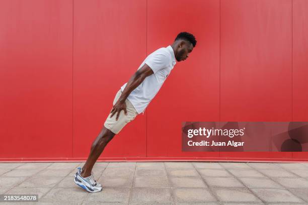 man moves forward in front of a bright red wall on a sunny day outdoors - leaning stock pictures, royalty-free photos & images