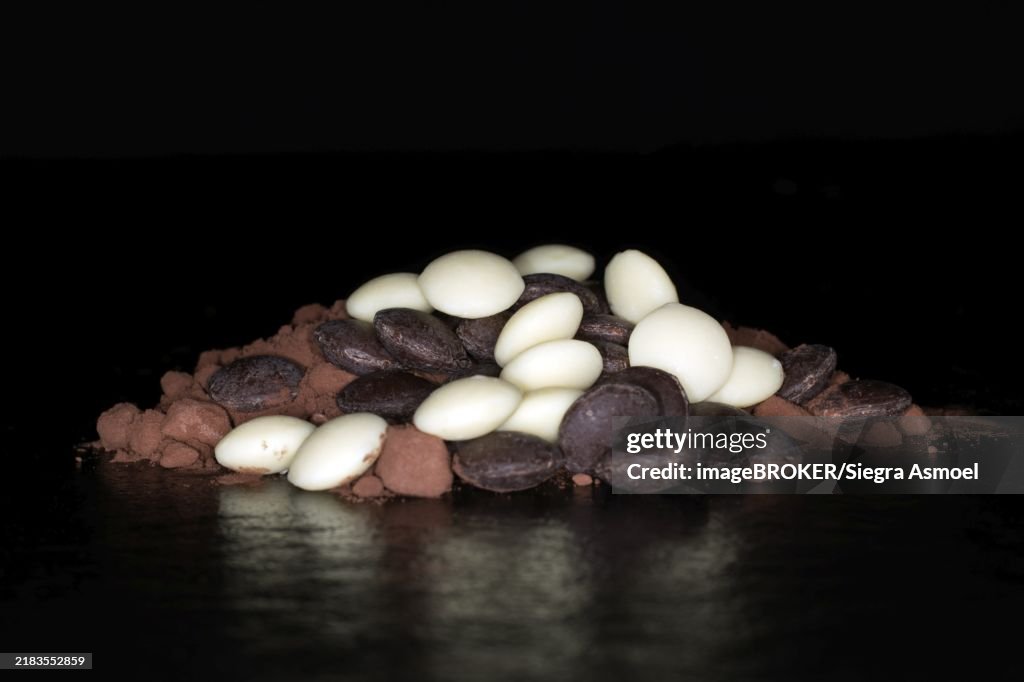 Dark and white couverture chocolate drops lying on cocoa powder, studio photography with black background
