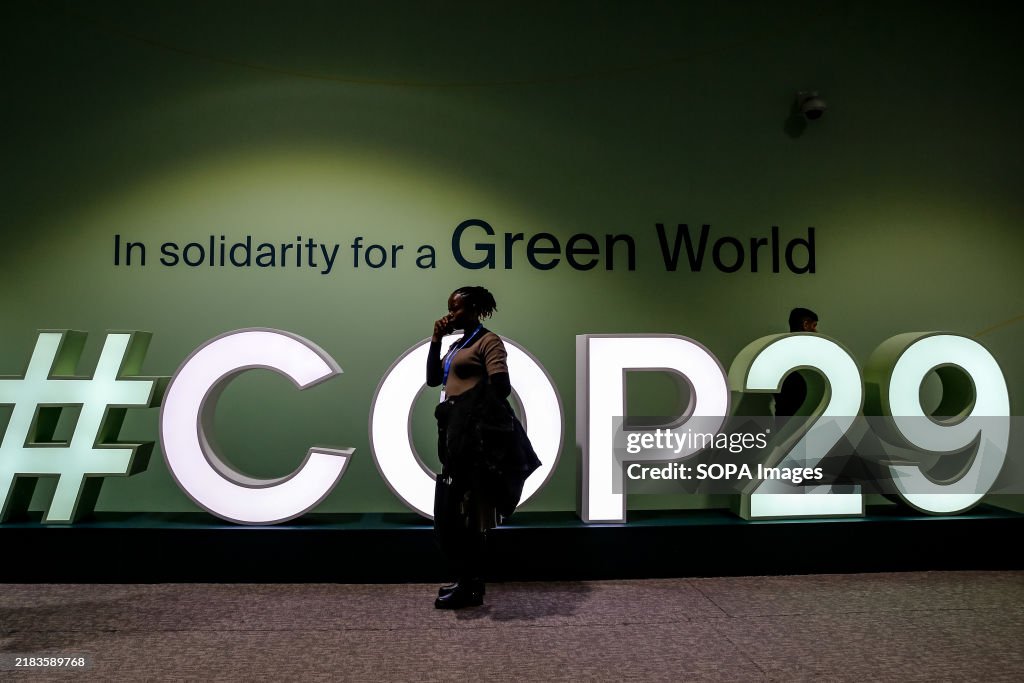 Participants walk past a logo of COP29, UN Climate Change...