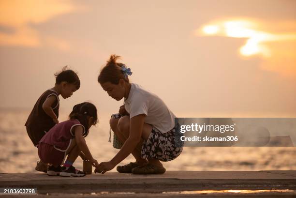 a mother playing with her two young children in silhouette against a vibrant beach sunset, capturing warmth and family connection. - single parent family silhouette stock pictures, royalty-free photos & images