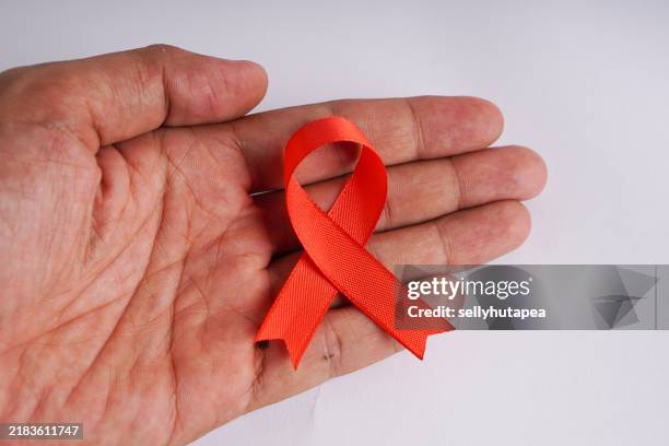 man holding red aids awareness ribbon in hands - preventive std stock pictures, royalty-free photos & images